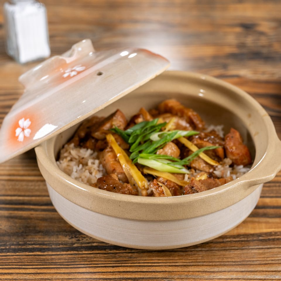 Vietnamese clay pot chicken and rice, garnished with green onions and ginger, on a wooden table.