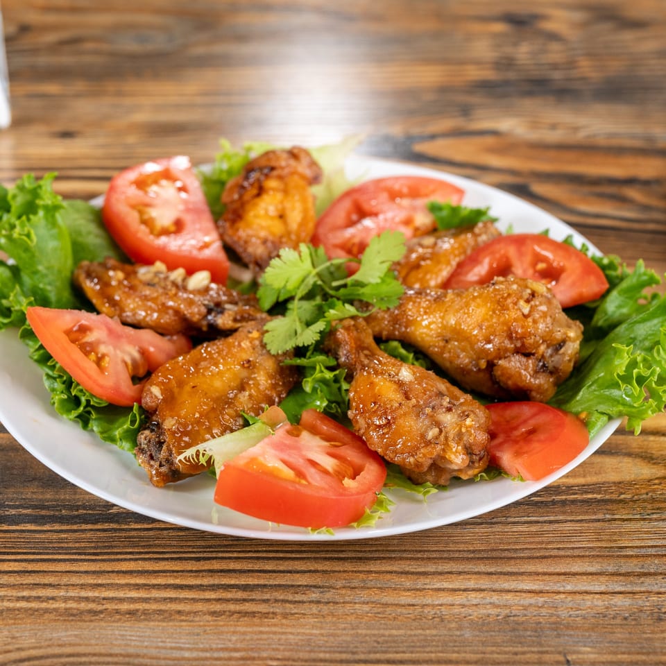 Crispy Vietnamese chicken wings with lettuce, tomato, and cilantro on a white plate.