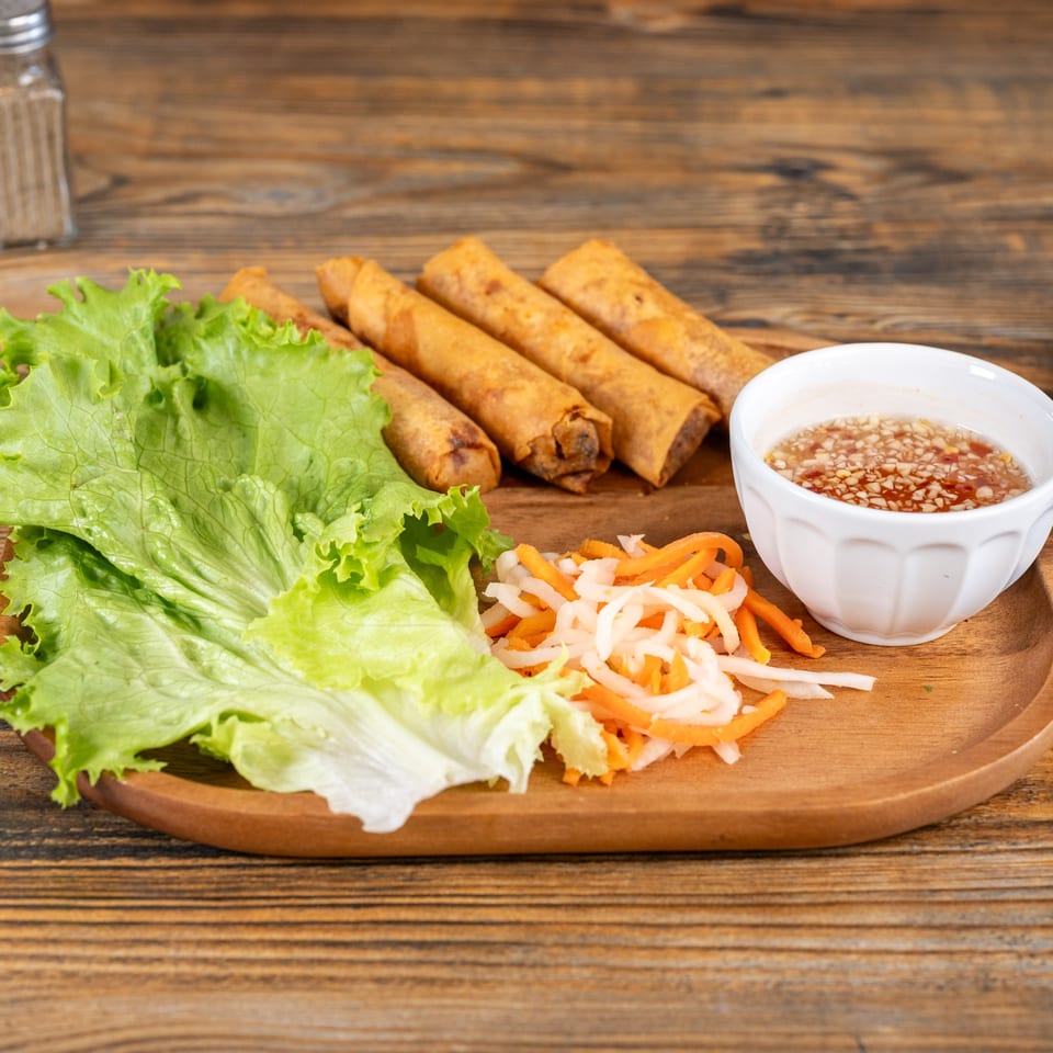 Crispy Vietnamese spring rolls with fresh lettuce, pickled vegetables, and a dipping sauce on a wooden plate.