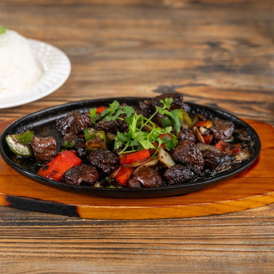 Sizzling beef cubes with red and green bell peppers, onions, and cilantro, served with rice.