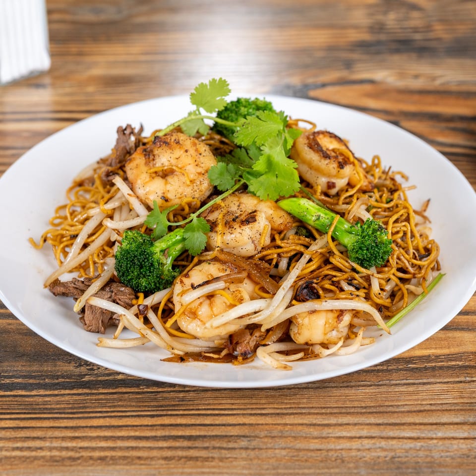 Vietnamese stir-fried noodles with shrimp, beef, broccoli, bean sprouts, and cilantro on a white plate.