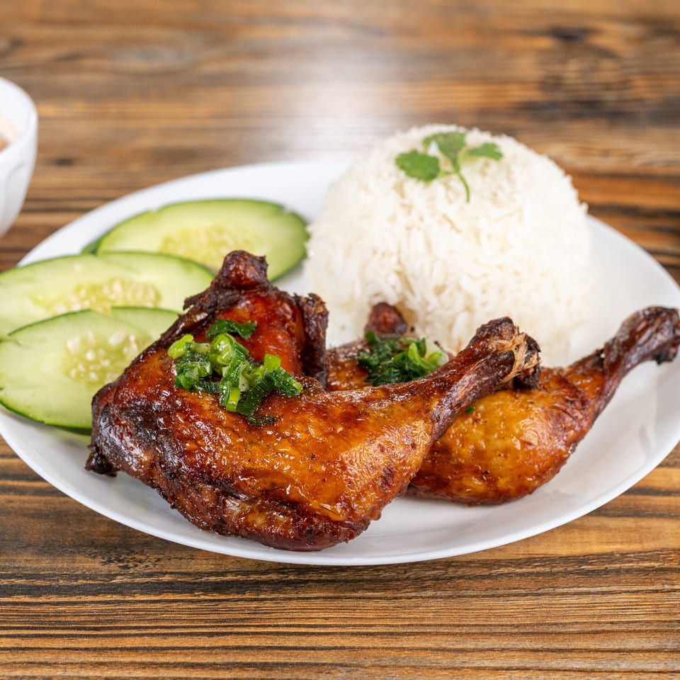 Grilled chicken legs with rice and cucumber slices on a white plate at Alpine Pho and Grill.